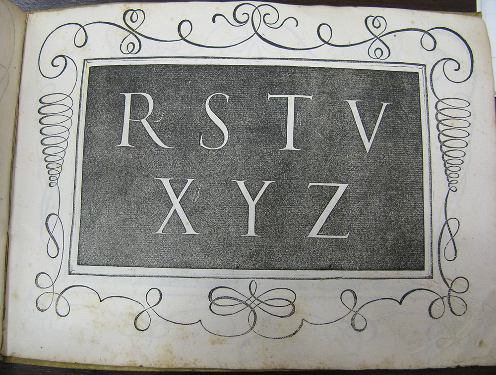 Stampa su carta realizzata con matrice in legno, che raffigura le lettere R, S, T, V, X, Y e Z in bianco su sfondo nero. Le lettere sono racchiuse all'interno di una cornice rettangolare. Il margine bianco della carta è decorato con motivi a spirale arzigogolati.
